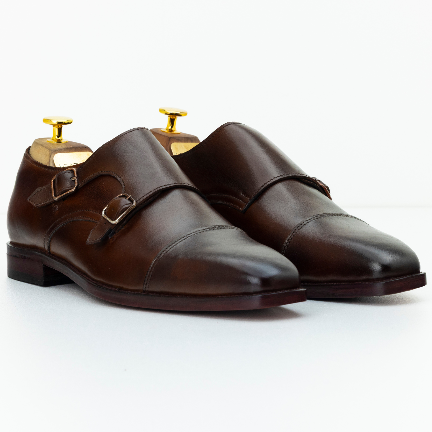 Pair of brown leather monk shoes with gold buckles on a white background