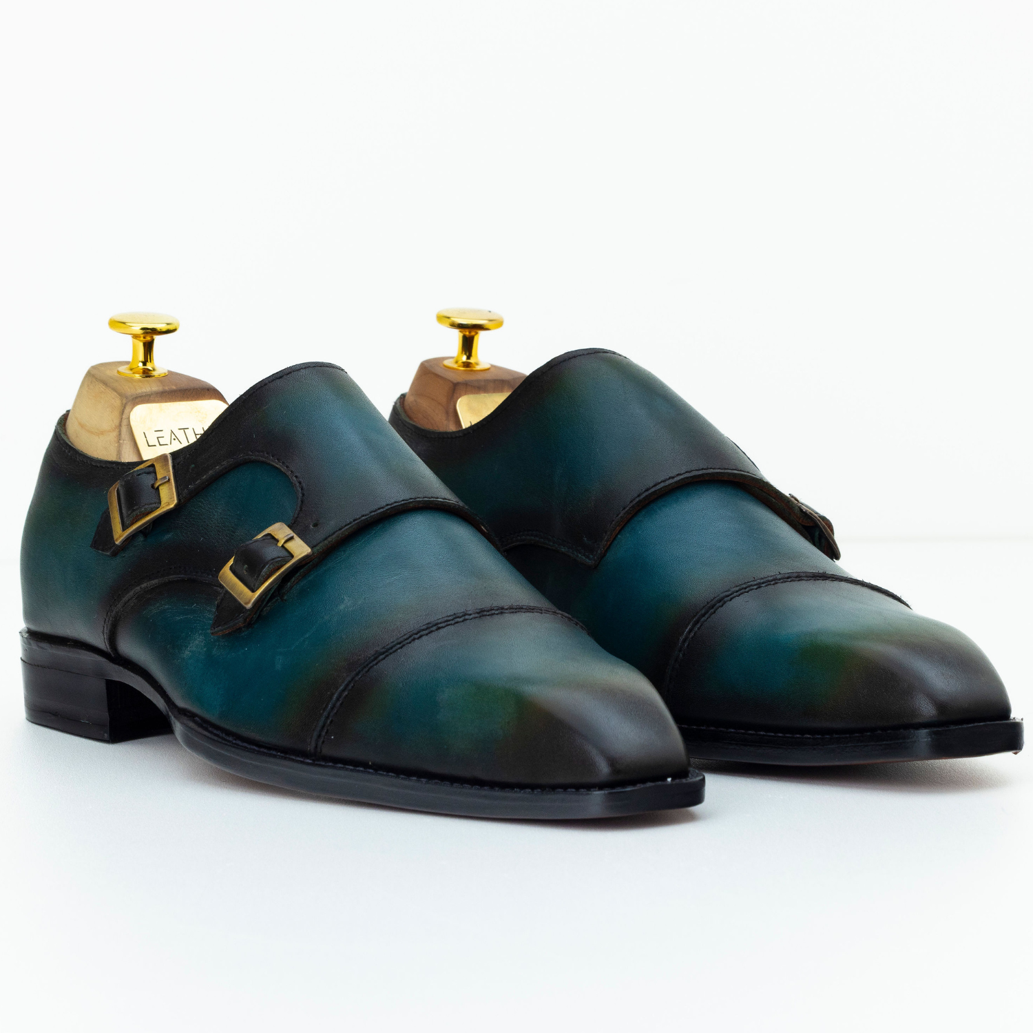 Pair of green leather shoes with gold buckles on a white background