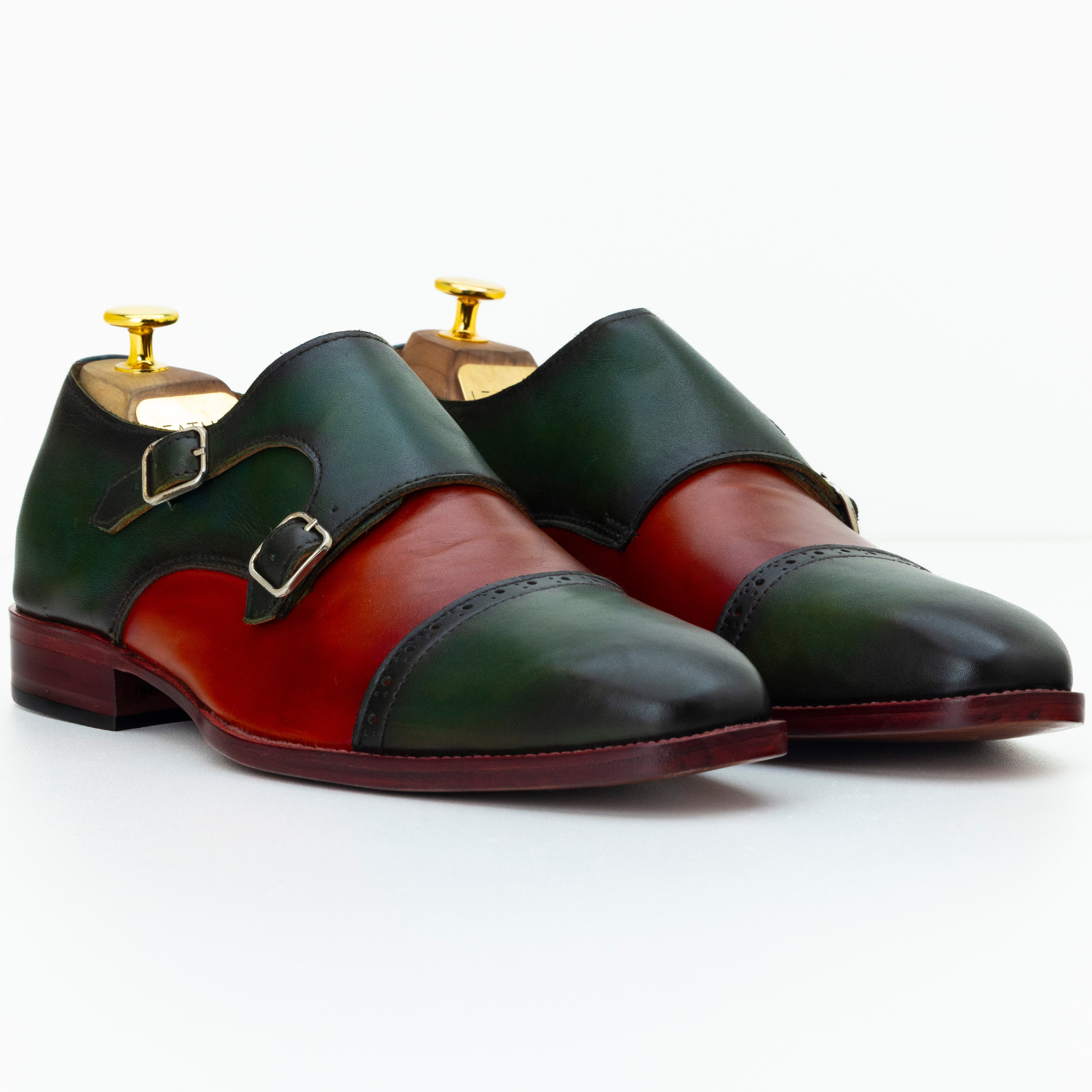 Pair of green and red leather shoes with gold buckles on a white background