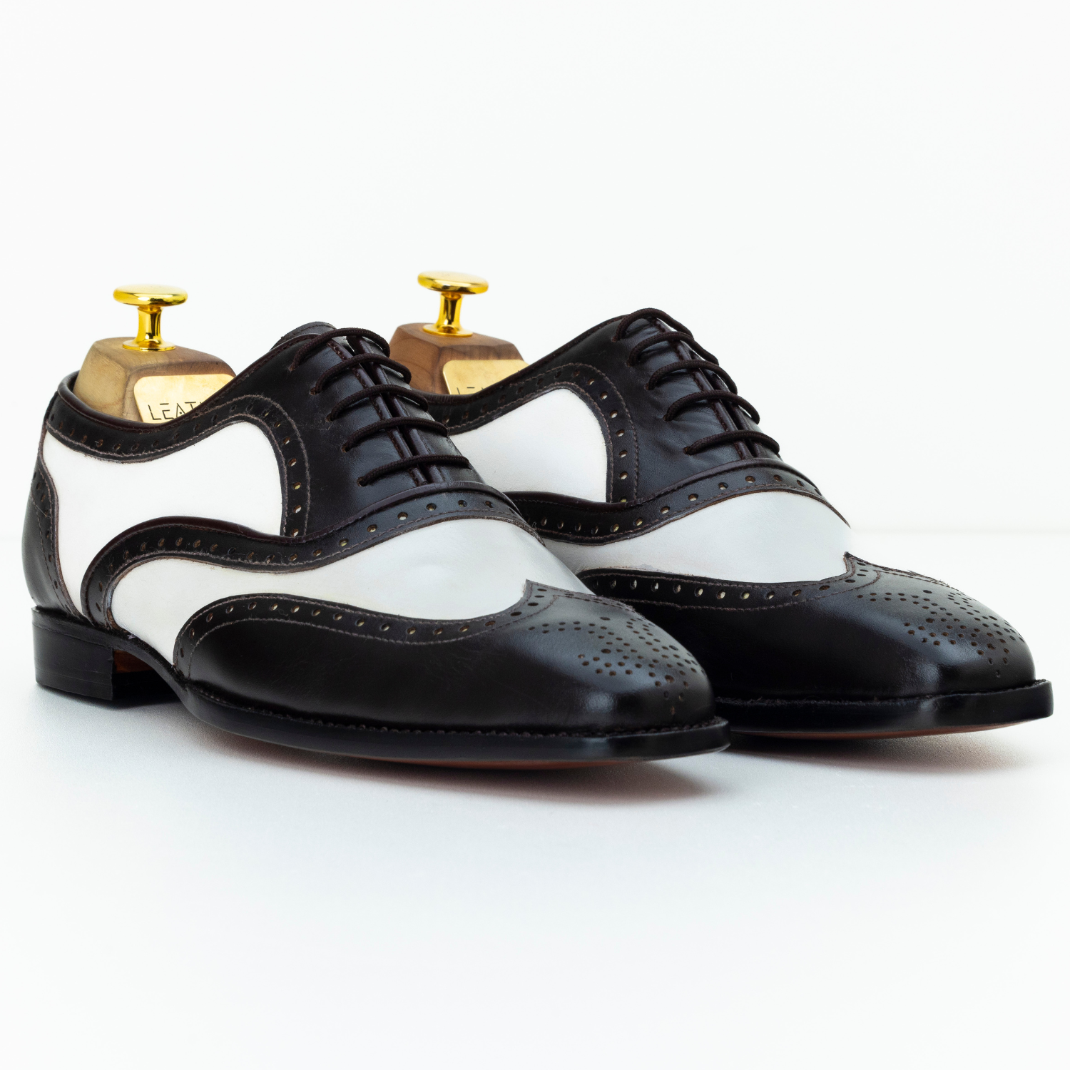 Black and white dress shoes with gold accents on a white background