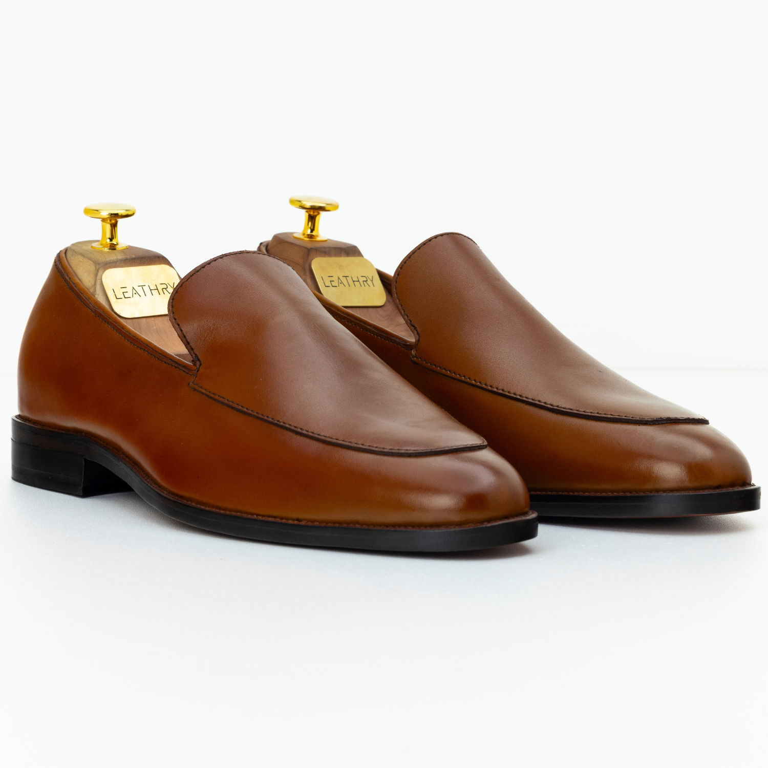 Pair of brown leather loafers with gold accents on a white background