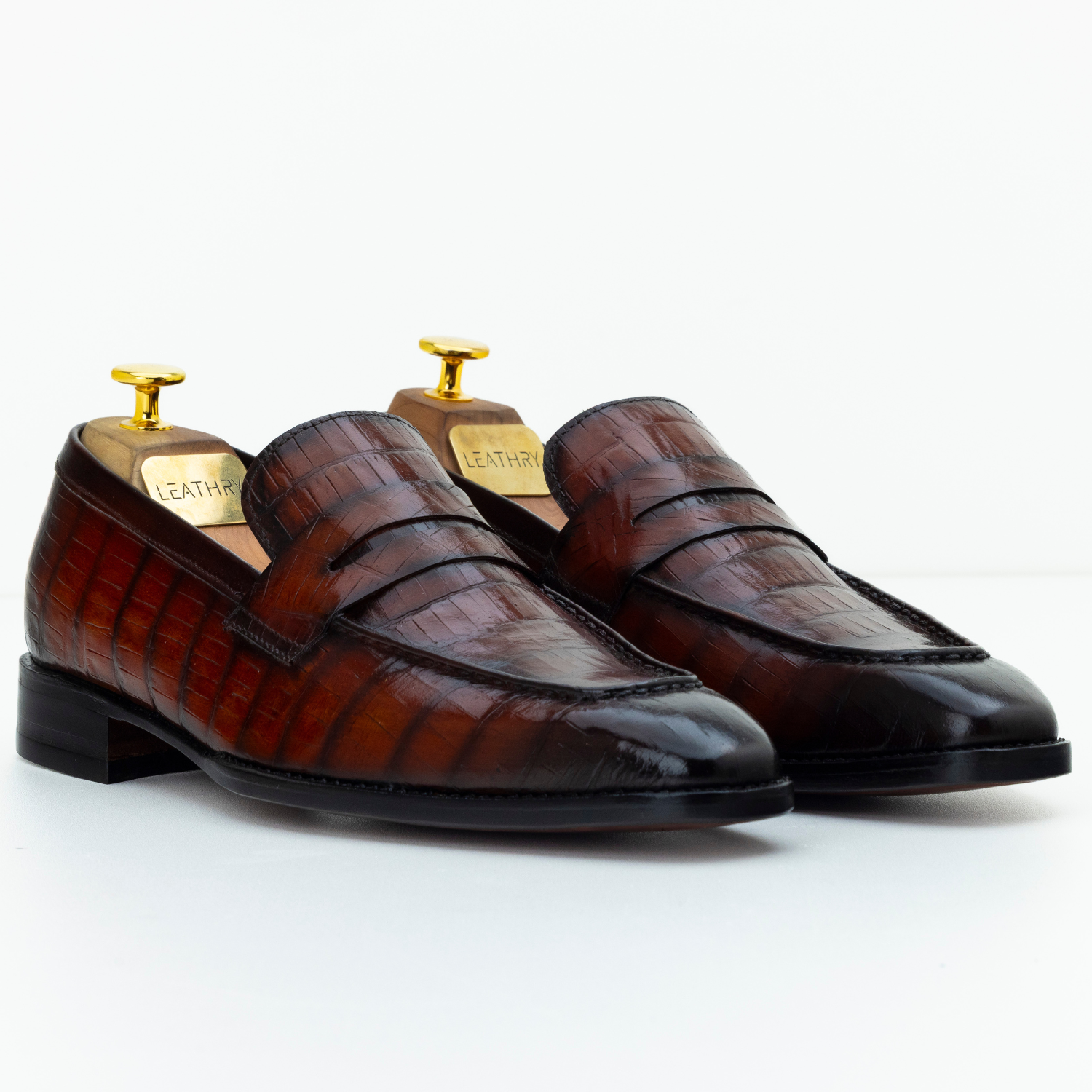 Pair of brown leather loafers with gold tags on a white background