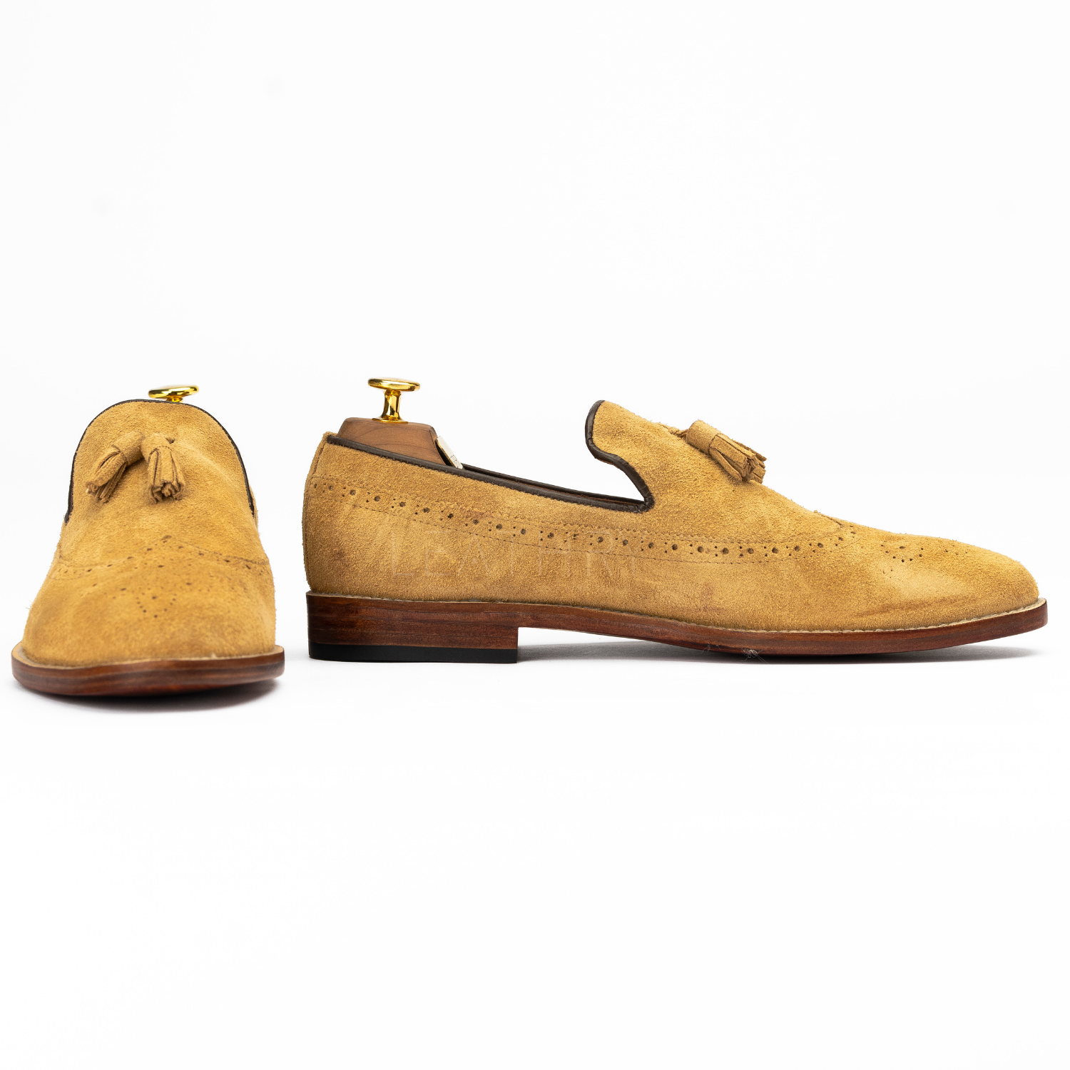 Pair of tan suede loafers with tassels on a white background