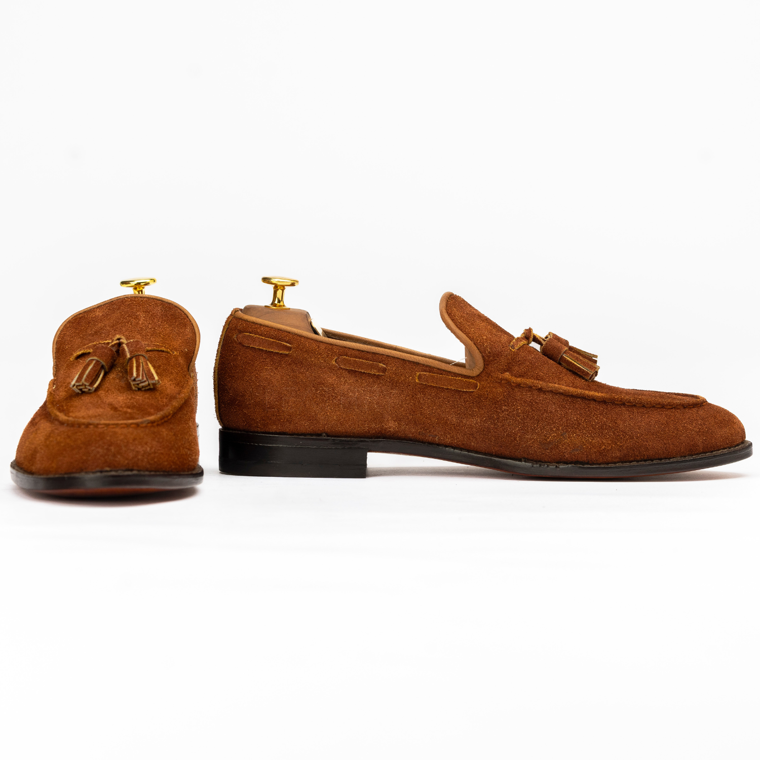 Pair of brown suede loafers with tassels on a white background