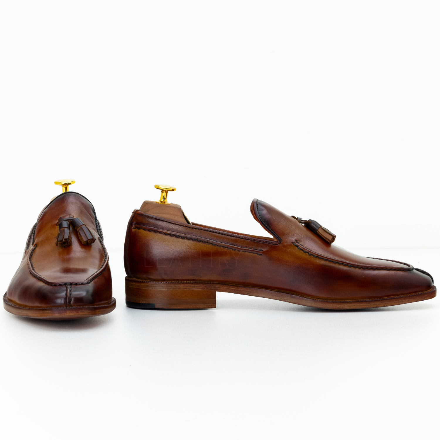 Pair of brown leather loafers with gold accents on a white background