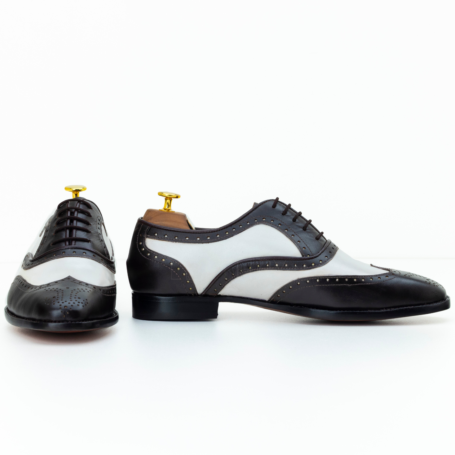 Black and white dress shoes with gold accents on a white background