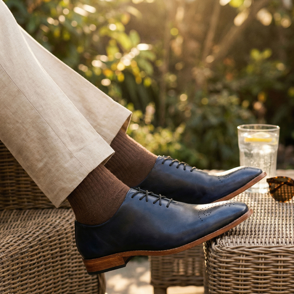 Person wearing dark blue leather shoes and brown socks sitting outdoors with a blurred natural background