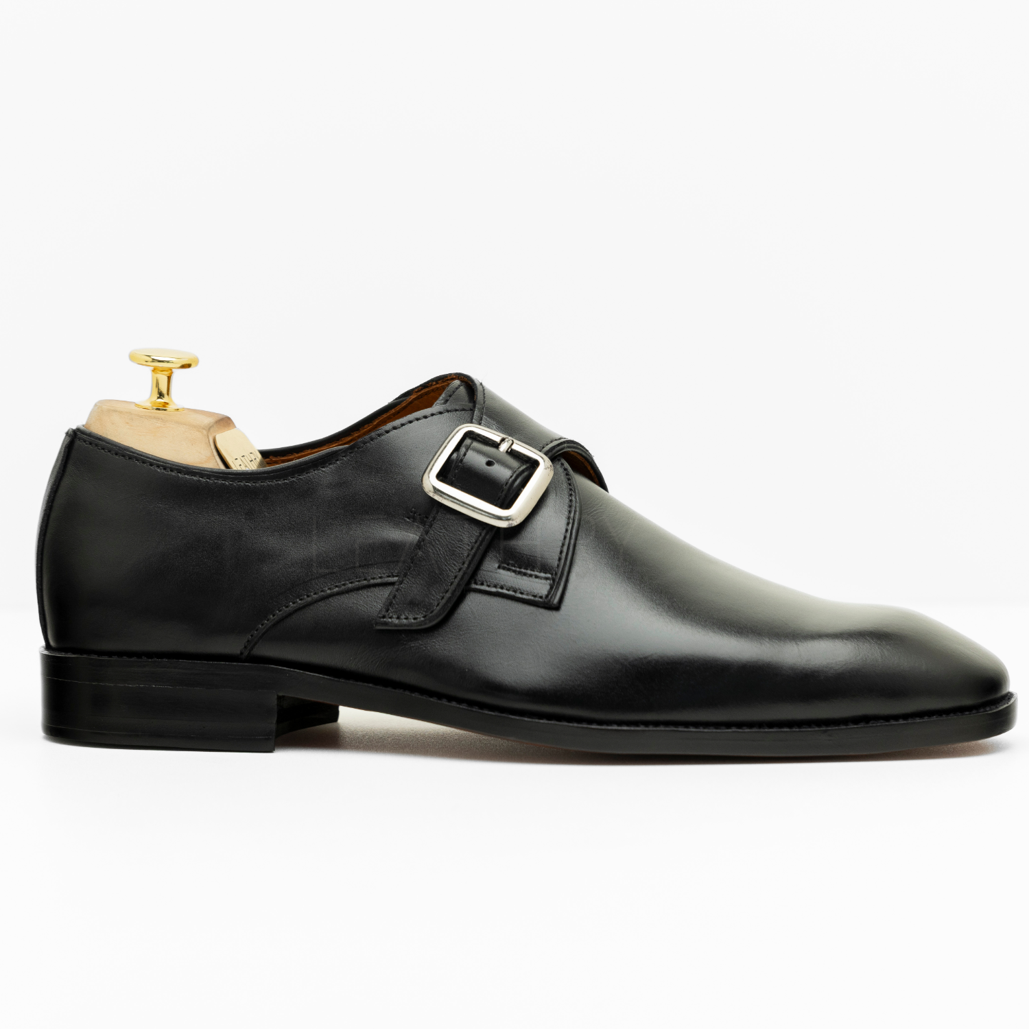 Black leather dress shoe with a buckle on a white background