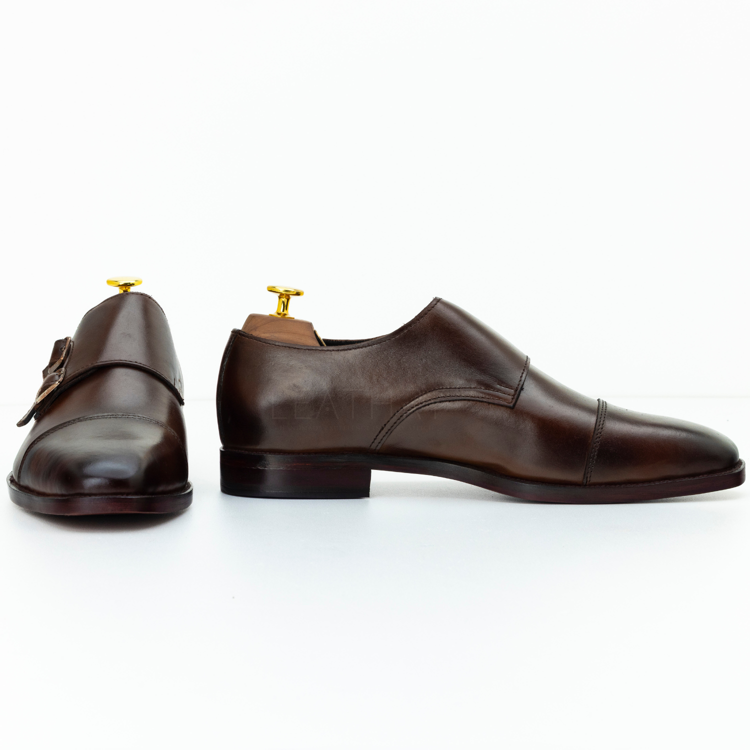 Pair of brown leather shoes with gold buckles on a white background