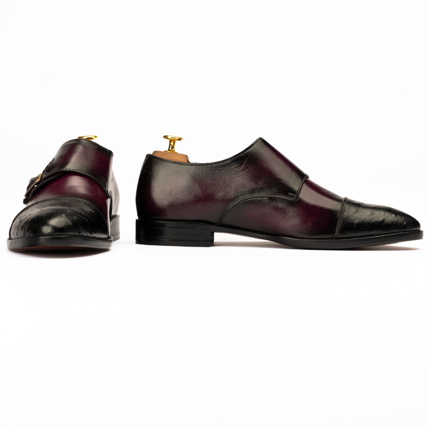 Pair of maroon leather shoes with gold buckles on a white background