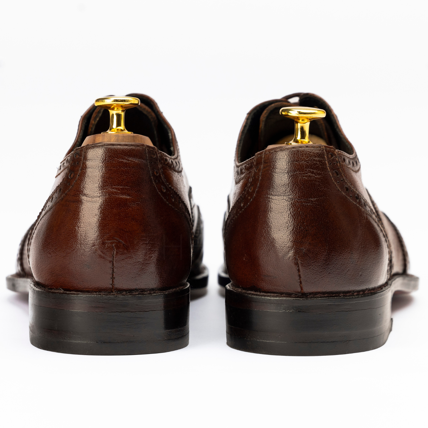 Brown leather dress shoes with gold dress studs on a white background