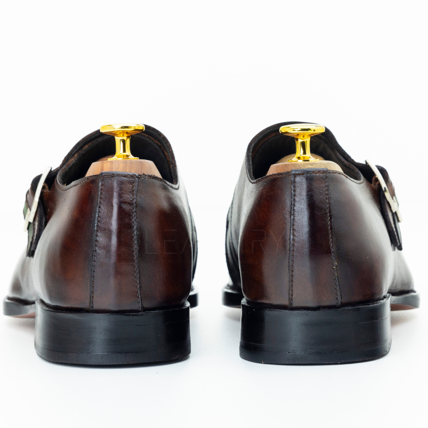 Brown dress shoes with gold accents on a white background