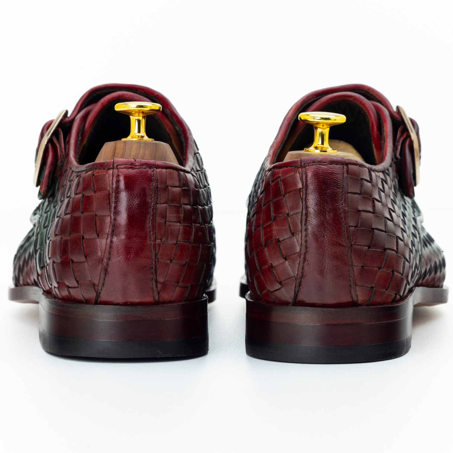 Pair of maroon leather shoes with gold buckles on a white background