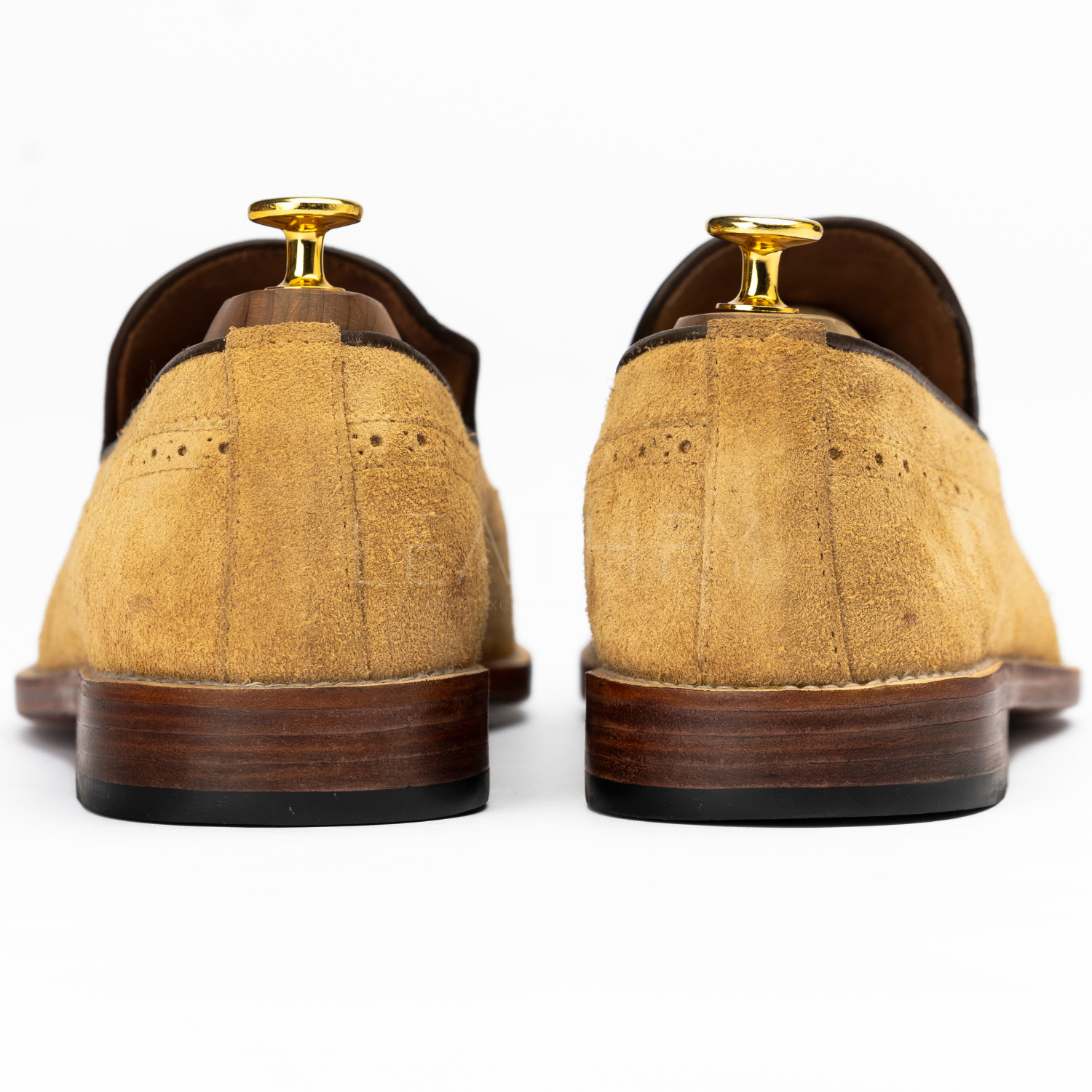 Pair of tan suede shoes with brown soles on a white background