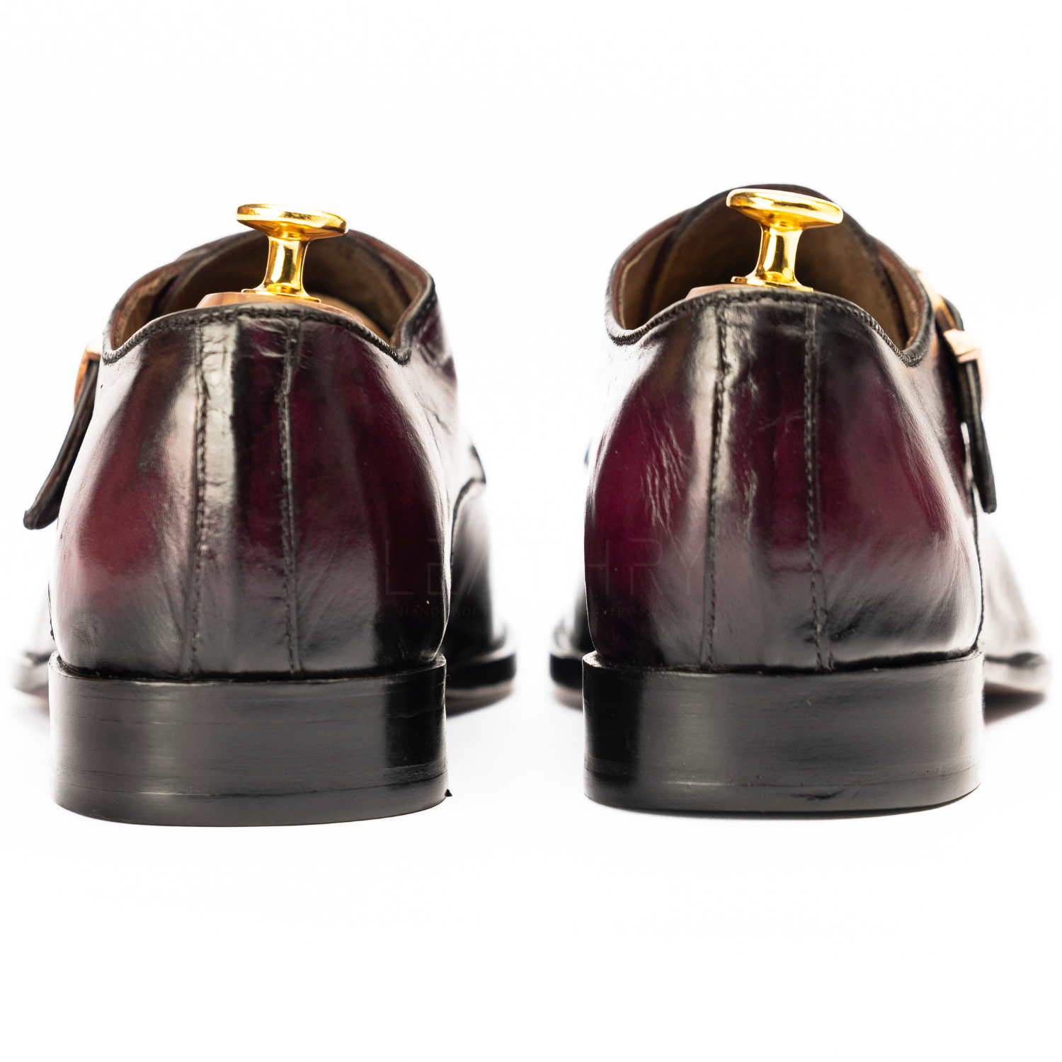 Pair of maroon leather shoes with gold accents on a white background