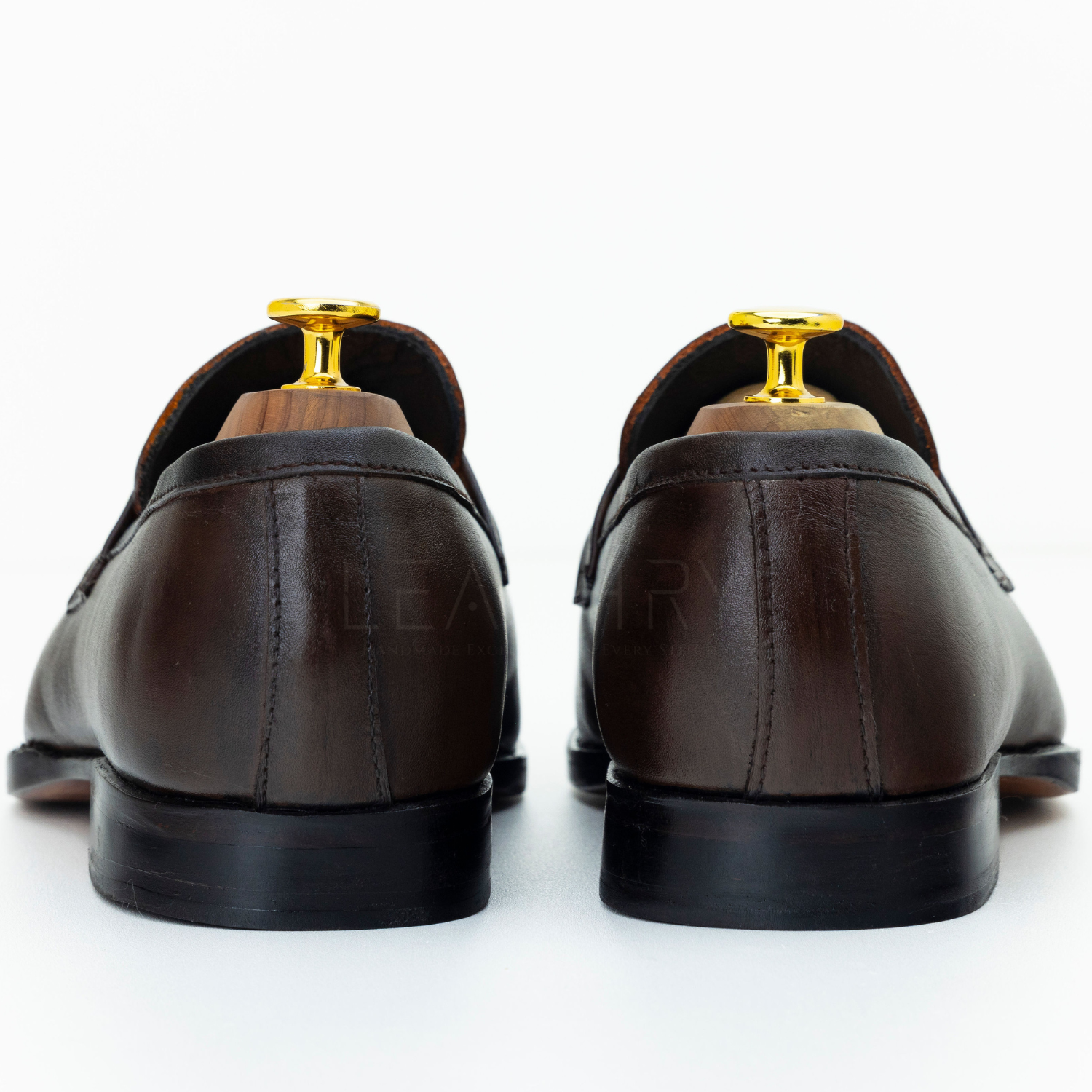 Brown leather loafers with gold accents on a white background
