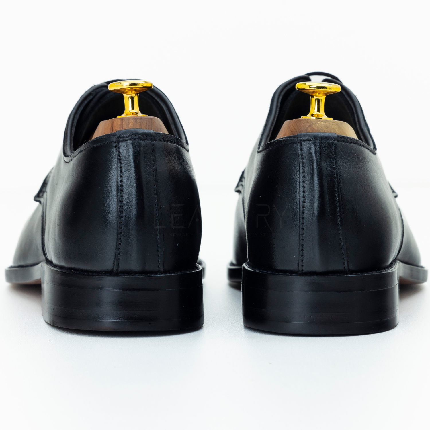 Black leather shoes with gold accents on a white background