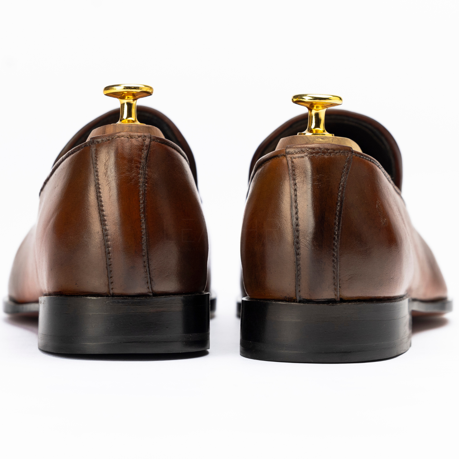 Pair of brown dress shoes with gold tips on a white background