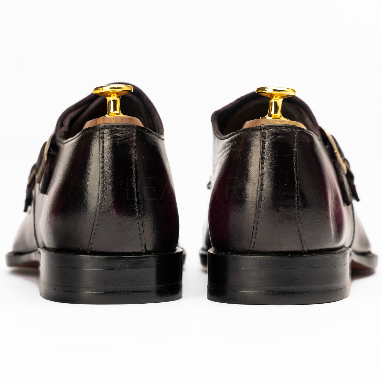 Black leather shoes with gold accents on a white background