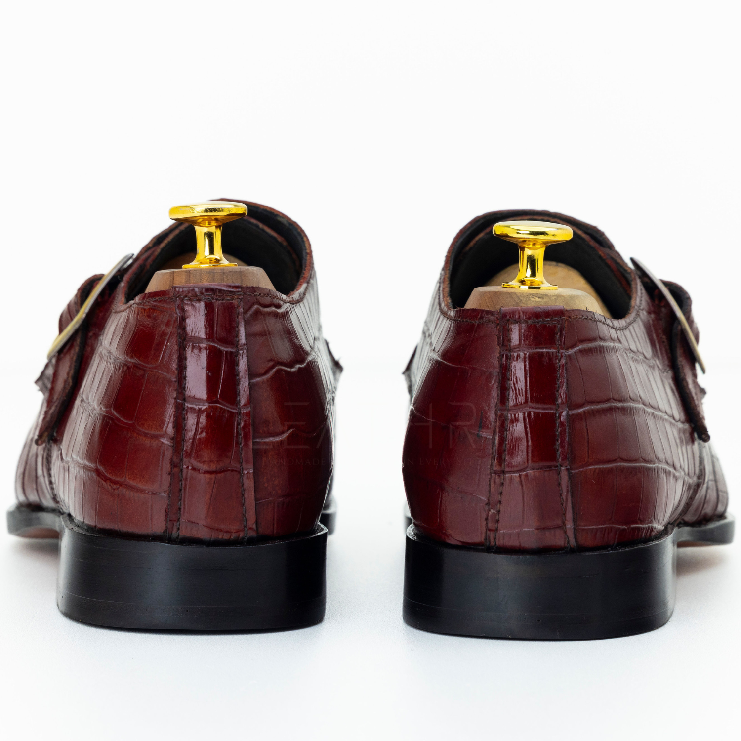 Brown crocodile-patterned shoes with gold accents on a white background