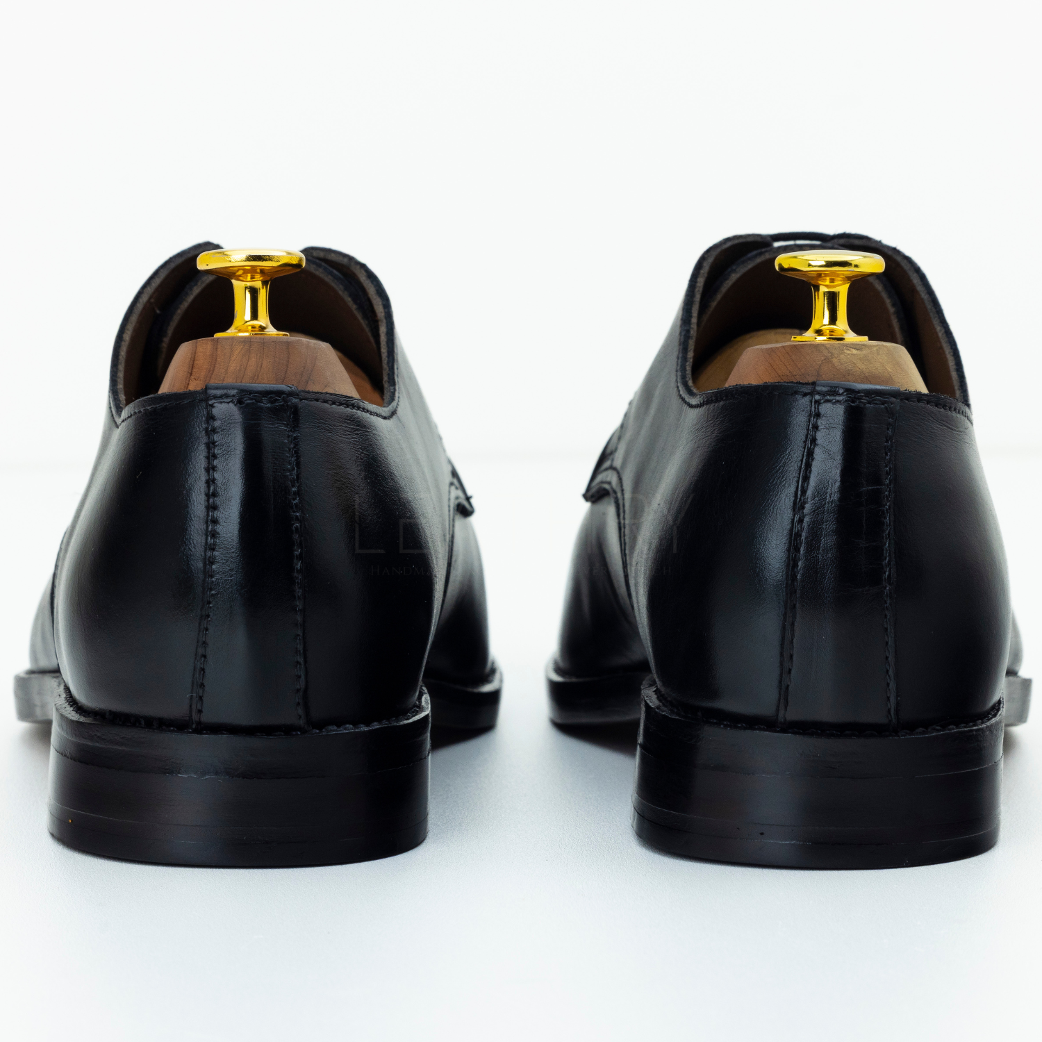 Black leather dress shoes with gold dress studs on a white background