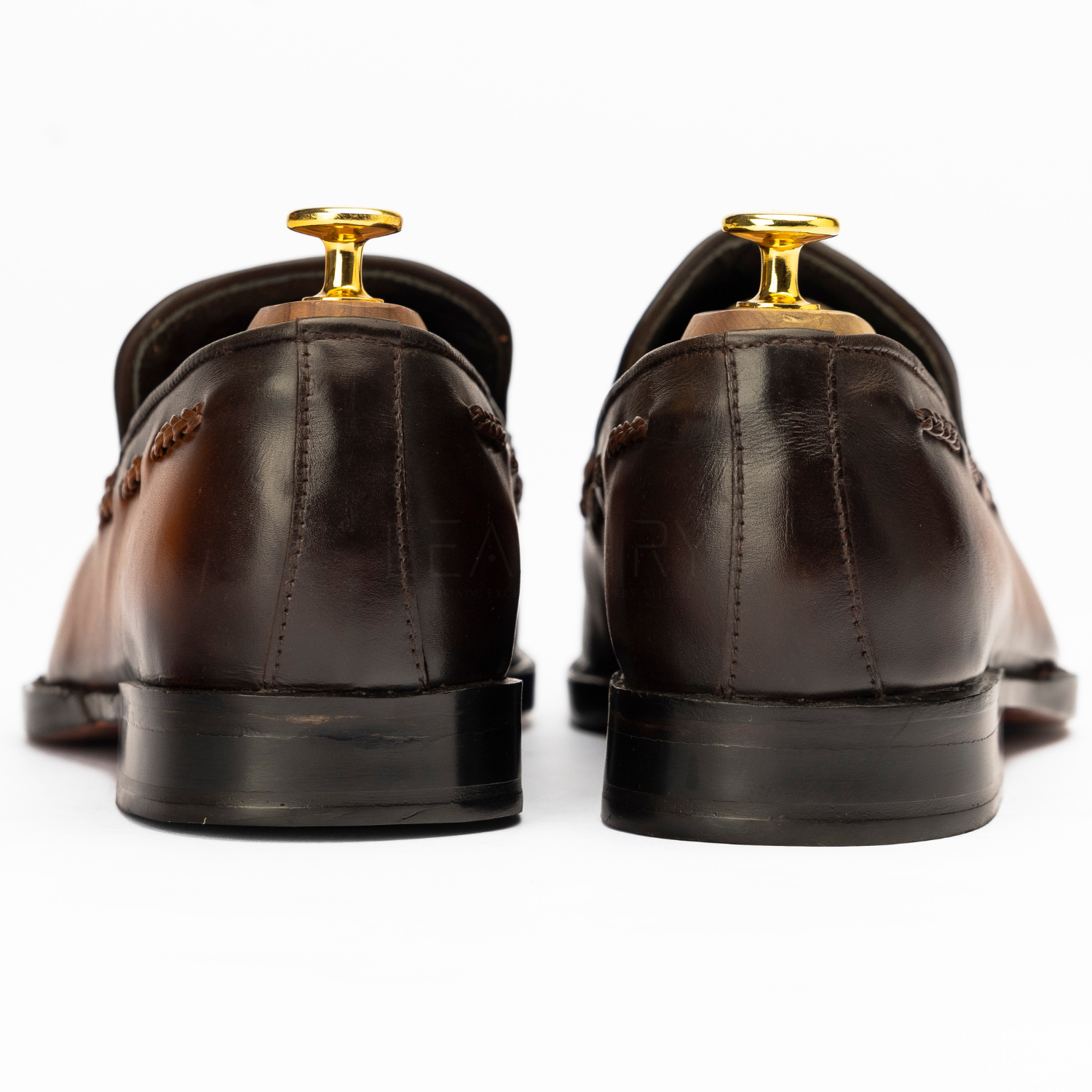 Pair of brown dress shoes with gold dress studs on a white background
