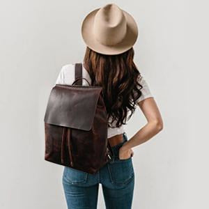 Person wearing a brown leather backpack and beige hat on a plain background