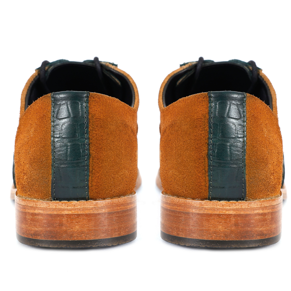 Brown suede shoes with black crocodile-patterned accents on a white background