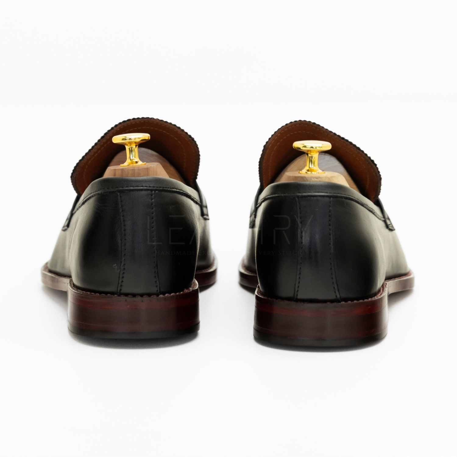 Pair of black leather loafers with gold buckles on a white background