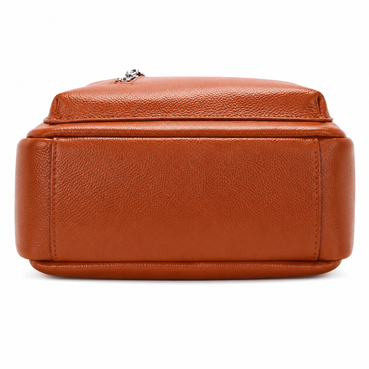 A close-up of the bottom front corner of a textured cognac brown leather bag, showing the pebbled grain, stitched edges, and a small silver metal zipper pull on a white background.