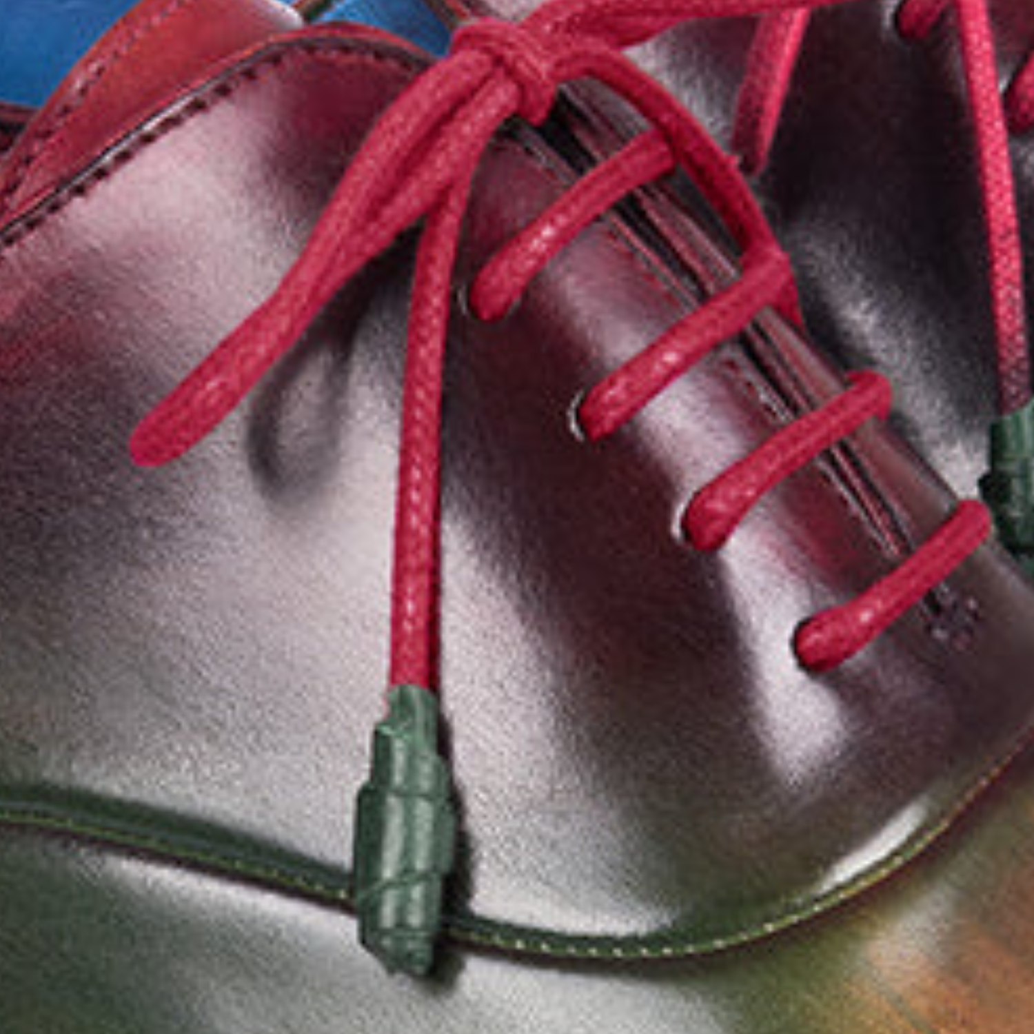 Close-up of a pair of maroon shoes with red laces on a wooden surface.