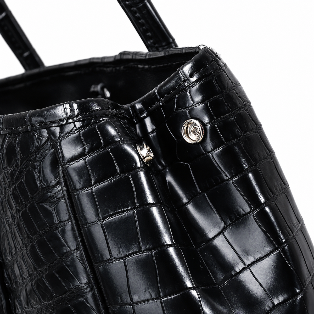 Close-up of a glossy black crocodile-embossed leather handbag with silver-tone hardware on a white background.