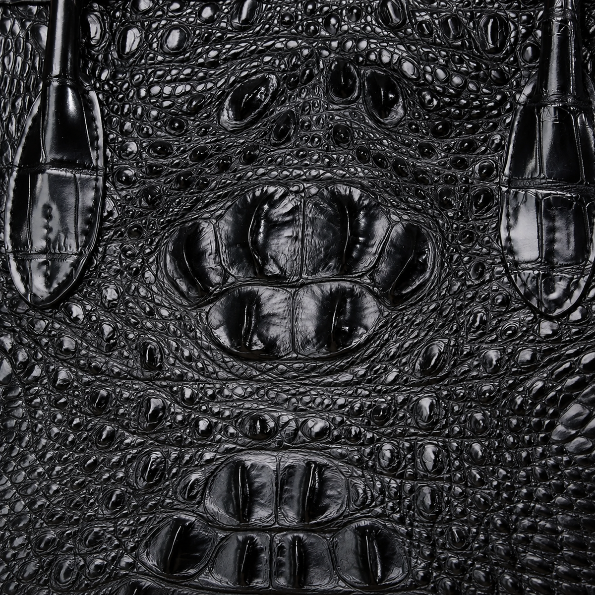 Close-up of black crocodile or alligator textured leather with raised scales and glossy highlights, filling the frame.