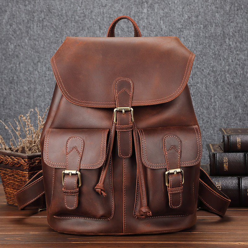 Brown leather backpack on a wooden surface with books and a basket in the background.