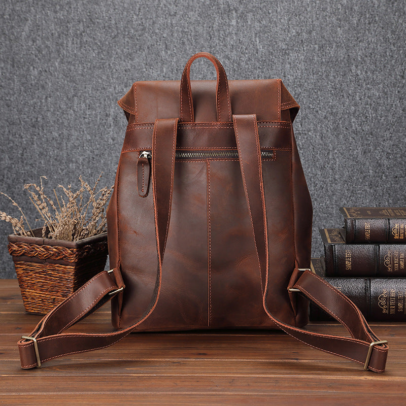 Brown leather backpack on a wooden surface with books and a plant in the background